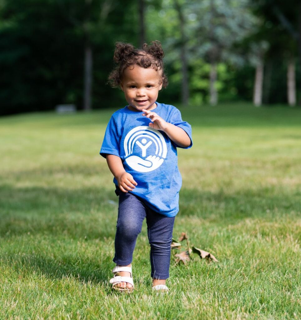 Toddler with curly black hair and dark skin walking towards the camera smiling wearing a United Way tshirt.