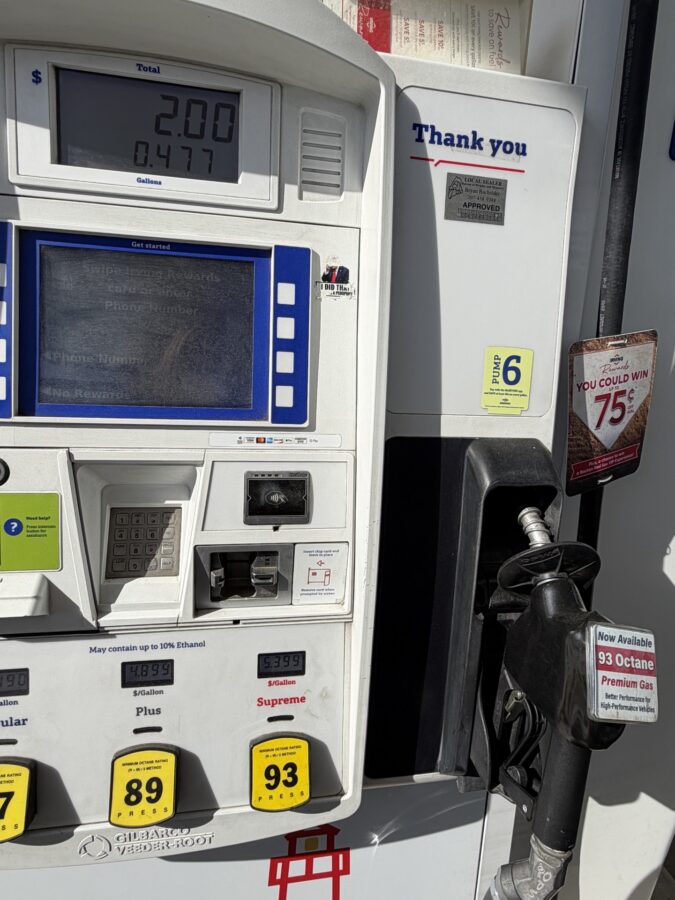 Gas pump payment terminal with a digital display showing 2.00 total and 0.477 gallons, beside a 'Thank you' sign at a fueling station