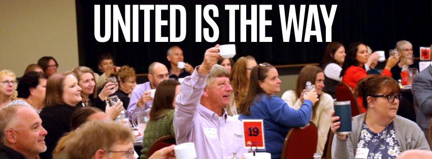 Crowd of diverse attendees at a banquet or conference, many raising cups in a toast, with a bold 'UNITED IS THE WAY' banner in the background.